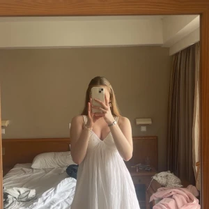 Vit kort sommarklänning med knyt - Supersöt vit kortklänning med v-ringning och smala axelband. Klänningen har knyt i midjan och faller lätt och luftigt, perfekt för varma dagar. Materialet känns tunt och skönt, och modellen är flowy och feminin.