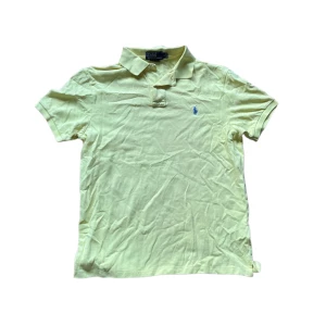 Ralph Lauren piké  - Snygg gul pikétröja från Ralph Lauren med klassisk krage och korta ärmar. Tröjan har blå broderad logga på bröstet och är gjord i mjuk bomull. Perfekt för en fräsch och avslappnad stil under varmare dagar. Se en liten defekt på sista bilden ! Jag skickar ej bild när jag bär plaggen och jag vet ej vilken längd och vikt de passar då jag inte prövar kläderna jag säljer 😃