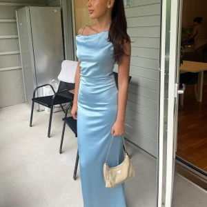 Adoore klänning - Endast använd 1 gång. Storlek 36. Supersnygg ljusblå långklänning i satin med smala axelband och elegant drapering vid bysten. Klänningen har en figurnära passform och en stilren, minimalistisk look som verkligen sticker ut. Perfekt för dig som vill ha en chic och modern stil.