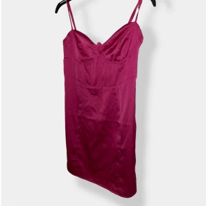 Rosa satin klänning från Nelly - Supersnygg rosa kortklänning från Nelly i glansigt satinmaterial. Klänningen har smala axelband, markerad byst och figurnära passform. Perfekt för dig som vill sticka ut med en färgstark look.