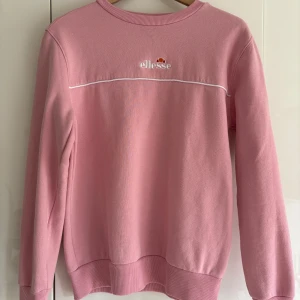 Rosa sweatshirt från Ellesse - Rosa sweatshirt från Ellesse med broderad logga på bröstet. Tröjan har rund hals, långa ärmar och ribbade muddar. Knappt använd. 