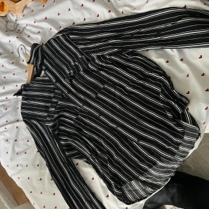 Svartvit randig skjorta med knappar - Snygg svart skjorta med vita ränder och klassisk krage. Skjortan har långa ärmar och knäppning framtill. Perfekt för dig som gillar en stilren och trendig look. Passar lika bra till jeans som till kostymbyxor.