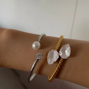 Silverarmband med pärla och sten - Stilrent armband i silverfärg med öppen design, prytt med en rund vit pärla på ena sidan och en gnistrande klar sten på den andra. Perfekt för dig som gillar minimalistiska och eleganta smycken med en modern twist.