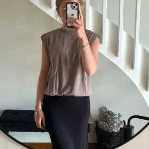 Beige ärmlöst linne   - Säljer en beige ärmlös topp med markerade axlar och rund halsringning. Toppen har en loose fit och är tillverkad i mjuk bomull, perfekt för en chill och trendig look. Enkel att styla med både jeans och kjol.