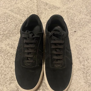 Axel Arigato skor - Snygga svarta sneakers från Axel Arigato i mocka med diskret logga på sidan. Skorna har svarta snören och en vit platt sula som ger en clean look. Perfekta för dig som gillar minimalistisk stil och vill ha något som funkar till det mesta. Priset kan diskuteras. 