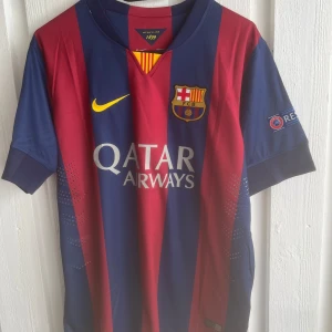 FC Barcelona Messi 10 matchtröja Nike - Barça fotbollströja med Messi 10 på ryggen. Klassiska blå och vinröda ränder, officiella klubbmärket och Champions League-patch på ärmen. Qatar Airways som sponsor framtill. Tillverkad i lätt och ventilerande material, perfekt för match eller träning.
