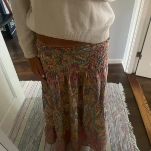 Färgglad långkjol från Marta - Säljer en bohemisk långkjol från Marta med färgglatt paisleymönster i rosa, blått, gult och grönt. Kjolen har smock i midjan för skön passform och är gjord i ett lätt och luftigt material, perfekt för varma dagar. Säljer för riktigt bra pris! Ny pris 600kr