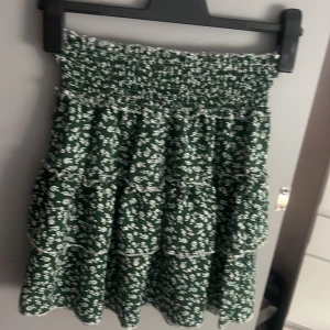 Grön blommig volangkjol - Supersöt grön kortkjol med vita blommor och flera volanger. Storlek S