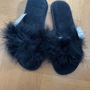 Svarta fluffiga sandaler från Rusta - Svarta sandaler med superfluffig pälsimitation över foten. Platt sula och öppen tå ger en chill vibe, perfekt för att glida runt hemma eller på sommaren. Märke: Rusta, modell Fia. Snyggt statement med den svarta färgen och den mjuka känslan.