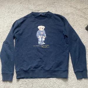 Blå sweatshirt Polo Bear Ralph Lauren - Mörkblå sweatshirt från Polo Ralph Lauren i storlek M med ikoniska Polo Bear-trycket på bröstet. Perfekt för dig som gillar klassisk streetstyle med en twist. Skriv vid fler frågor😁