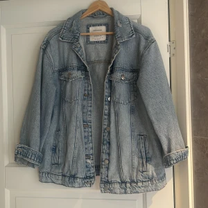 Oversized ljusblå jeansjacka från Stradivarius - Säljer en oversized ljusblå jeansjacka från Stradivarius. Jackan har klassisk krage, knappar framtill, två bröstfickor med lock och två sidofickor. Snygga slitningar och avslappnad passform gör den perfekt till din streetstyle.