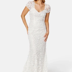 Gigi dress från Ida Sjöstedt färg Ivory, storlek 34 - Helt ny, aldrig använd, vit långklänning med v-ringning, korta ärmar i spets och 3D-blommor över hela klänningen. Sitter figurnära och har romantiska detaljer som gör den perfekt för speciella tillfällen.