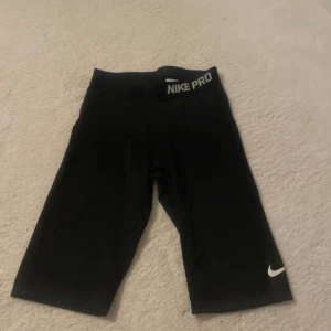 Svarta Nike Pro träningstights shorts - Svarta cykelshorts från Nike Pro med vit logga på benet och bred resår i midjan. Tight passform och stretchigt material som passar perfekt till träning eller sport. Klassisk och stilren design med diskret Nike Pro-tryck i midjan.