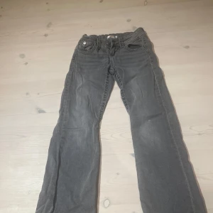 Grå jeans med broderade bakfickor - Säljer ett par grå jeans med snygga broderade detaljer på bakfickorna. Byxorna har klassisk femficksdesign och raka ben. Perfekta för dig som gillar en chill och stilren look. Dom har en liten bleknings fläck på ena benet.