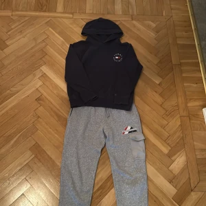 Grå mjukisbyxor Tommy Hilfiger - Snygga grå mjukisbyxor från Tommy Hilfiger med broderad logga och cool cargo-ficka på ena benet. Byxorna har snörning i midjan och muddar vid bensluten för en skön och avslappnad passform. Perfekta för chill dagar eller streetwear-stil.