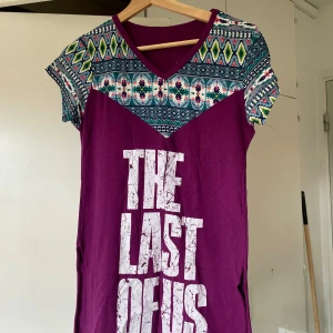 Lila t shirt The Last of Us - Cool lila t shirt. Överdelen och ärmarna har färgglatt etnoinspirerat mönster i blått, grönt, gult och rosa. V-ringad hals och korta ärmar. Perfekt för dig som vill sticka ut med en unik stil.