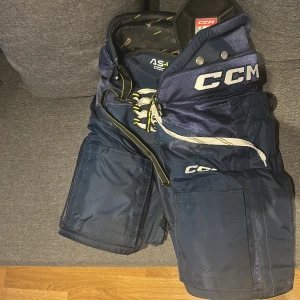 CCM AS-V Pro hockeybyxor marinblå M - Säljer ett par marinblå CCM AS-V Pro hockeybyxor i storlek medium. Byxorna har snörning i midjan, extra vaddering och robust konstruktion för att skydda under match och träning. Snygg design med tydlig CCM-logga och justerbar passform. PRIS KAN DISKUTERAS SJÄLVKLART 