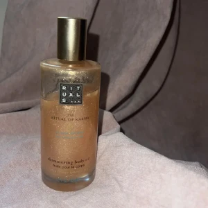 Rituals The Ritual of Karma Shimmer Oil - Rituals The Ritual of Karma Shimmering Body Oil i en lyxig glasflaska med guldfärgat lock. Oljan har en varm gyllene ton med massor av skimrande glitter som ger huden en snygg glow. Innehåller lotusblomma och vitt te för en fräsch doft.