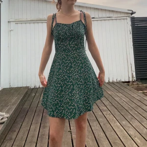 Grön blommig kortklänning med knyt - En fin blommig sundress med ett tunt skönt tyg, har en fin längd och knytning går att justera hur man vill