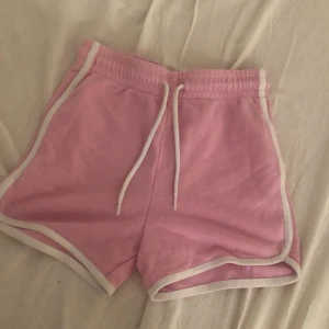 Rosa sportiga shorts med snörning - Snygga rosa shorts med vita kanter och snörning i midjan. De har en sportig retrostil och är perfekta för varma dagar. Mjukt material och elastisk midja gör dem riktigt bekväma att ha på sig.