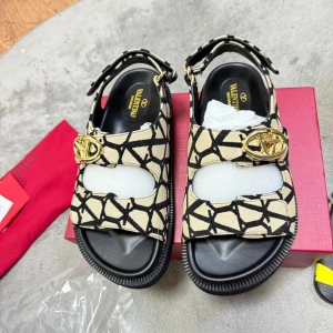 Valentin Garavani sandaler med mönster - Snygga sandaler från Valentin Garavani i beige och svart med grafiskt mönster och guldfärgade logodetaljer. Skorna har öppen tå, platt sula och justerbar rem med spänne. Perfekta för att lyfta din sommarstil med en lyxig touch.