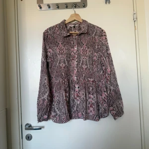 Mönstrad rosa skjorta  - Supersnygg skjorta med unikt grafiskt mönster i rosa, svart och beige. Skjortan har knappar framtill, klassisk krage och lång ärm med resår vid ärmslut. Luftig och flowy passform som ger en chill vibe. Från märket Odd Molly i storlek 2 som enligt deras storleksguide motsvarar en storlek M. Mycket fint skick, jag hittar inga synlig anmärkningar eller defekter.  