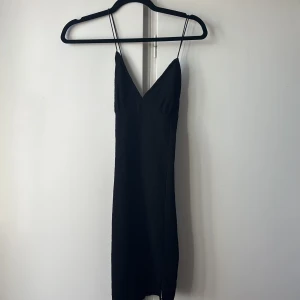 Svart kort klänning med tunna band - Supersnygg svart kort klänning med tunna axelband och v-ringning. Klänningen har öppen rygg med korsade band och en lätt strukturerad yta. Perfekt för dig som gillar minimalistisk och stilren look. Hör av dig om du vill ha fler bilder eller har några frågor! 