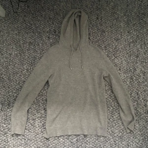 Grå Kashmir hoodie - En stilren grå hoodie med snörning i huvan och långa ärmar. Tröjan är i mjukt material och har en klassisk passform som funkar till många olika outfits. Perfekt för dig som gillar en enkel och clean look.
