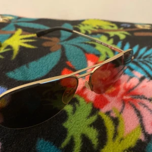 Guldiga aviator-solglasögon Michael Kors - Snygga aviator-solglasögon från Michael Kors, modell MK 1001 Gramercy. Guldiga metallbågar med mörka, lätt tonade linser. Klassisk pilotform som ger en cool vibe och passar till de flesta outfits. Perfekta för soliga dagar när du vill sticka ut lite extra.