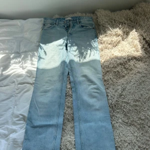Ljusblå raka jeans från Zara - Säljer ett par ljusblå jeans från Zara med raka ben och hög midja. Jeansen har klassisk femficksdesign, knäppning med flera knappar och råa kanter vid fickorna. Perfekta för en chill och trendig look. Skulle säga att byxorna sitter mer mid än High. 