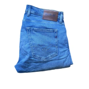 Replay Grover jeans blå, stl 34/32 - Säljer ett par Replay Grover jeans i klassisk blå tvätt. Jeansen har raka ben, fem fickor och snygga detaljer på bakfickorna. Tillverkade i ekologisk bomull för en skön känsla och stilren look. Perfekta för dig som gillar en tidlös jeansstil se vänsterbakficka på sista bilden !.Jag skickar ej bild när jag bär plaggen och jag vet ej vilken längd och vikt de passar då jag inte prövar kläderna jag säljer 😃