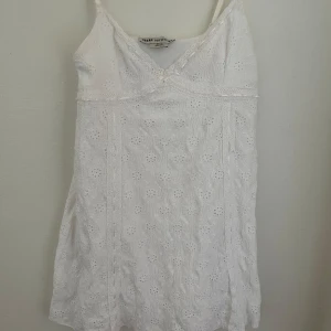 Vit spetsklänning Urban Outfitters - Superfin vit kortklänning från Urban Outfitters med broderad spets och tunna axelband. Klänningen har v-ringning, liten rosett framtill. Storlek XL men är omsydd att passa en S bättre. 