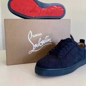 Mörkblå sneakers från Christian Louboutin kan gå med på mindre pris  - Exklusiva mörkblå sneakers från Christian Louboutin i mocka med den ikoniska röda sulan. Skorna har rund tå, snörning och en stilren design som sticker ut. Perfekta för dig som vill ha något unikt och lyxigt i garderoben.