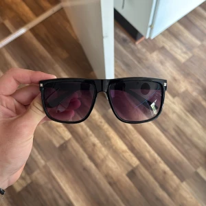 Svarta solglasögon rayban boyfriend liknande - Snygga solglasögon med svart, fyrkantig båge och lila tonade glas. Stilren och modern design som passar perfekt till sommaren. Bågarna är i plast och har en cool vibe som lyfter vilken outfit som helst. De ser ut som rayban boyfriends. Jätte snygga. Herr glasögon