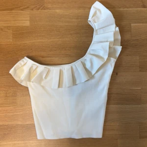 Vit oneshoulder topp med volang från Zara - Superfin vit topp med oneshoulder-design och bred volang längs halsringningen. Jättepopulär från Zara i nyskick ❣️