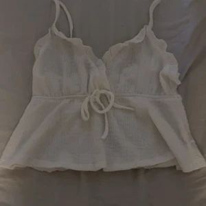 Vit topp från SHEIN - Supersöt vit topp från SHEIN med smala axelband, volangkant vid bysten och knyt i midjan. Perfekt för varma dagar och ger en romantisk vibe. Så gullig, dock förliten för mig. Sitter som en M men passar även S. 