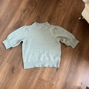 Mintgrön stickad tröja med puffärm - Superfin mintgrön stickad tröja med ribbad hals, ärmslut och nederkant. Tröjan har kortare puffärmar som ger en trendig look och är perfekt för lager-på-lager. Enkel att matcha med både jeans och kjol.