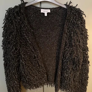 Svart glittrig kofta från & Other Stories - Säljer en unik svart kofta från & Other Stories med glittriga detaljer. Koftan har en fluffig textur och är perfekt för att ge din outfit en extra touch. Den är öppen framtill och har långa ärmar. Perfekt för kyliga kvällar eller när du vill sticka ut lite extra.