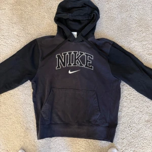 Svart hoodie från Nike - Säljer en svart hoodie från Nike med stor logga på bröstet. Tröjan har en klassisk känguruficka och justerbar huva med dragsko. Perfekt för en avslappnad stil. Storlek M. Mycket bra skick