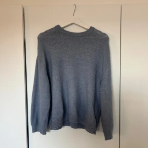 Grå stickad tröja - Säljer en mysig grå stickad tröja med rund hals och långa ärmar. Perfekt för kyliga dagar och enkel att matcha med olika outfits. Tröjan har ribbstickade muddar vid ärmslut och nederkant.