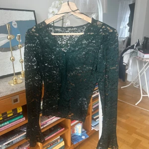 Grön spetsblus från Gina Tricot - Säljer en elegant grön spetsblus från Gina Tricot. Blusen har långa ärmar och en vacker spetsdesign som ger en romantisk känsla. Perfekt för att klä upp vilken outfit som helst. Tillverkad av återvunnen polyamid och elastan för en bekväm passform.