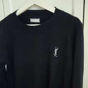 Svart YSL tröja - Svart YSL tröja, storlek XS-S. Tröja med  broderad logga på bröstet. Tröjan har en klassisk rund halsringning och långa ärmar. Perfekt för en stilren look. Ny, aldrig använd.