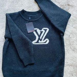 Svart tröja från Louis Vuitton - Säljer en stilren svart tröja från Louis Vuitton med det ikoniska LV-logotypen i vitt på framsidan. Tröjan har en rund halsringning och långa ärmar, perfekt för en trendig look.