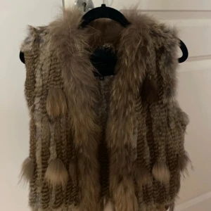 Brun pälsväst från Hollies - Säljer en lyxig brun pälsväst från Hollies. Västen har en mjuk och fluffig textur med ett stilrent mönster. Perfekt för att hålla sig varm och trendig under kyliga dagar. Passar utmärkt till både vardag och speciella tillfällen. Priset kan diskuteras! 