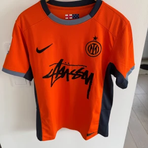 Inter x Stussy fotbollströja  - Säljer en Inter X Stussy  fotbollströja från Nike med svart tryck och detaljer. Tröjan har korta ärmar och en Serie A-logga på ärmen. Perfekt för fotbollsfans som vill ha något unikt och stilrent. Tröjan är knappt använd och är i absoluta nyskick, tröjan är också unik och svår att få tag på! 