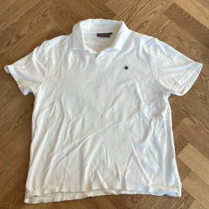 Vit kortärmad pikétröja från Morris - Säljer en stilren vit pikétröja från Morris med korta ärmar och en klassisk krage. Tröjan har en liten broderad detalj på bröstet och är tillverkad i ett mjukt material.