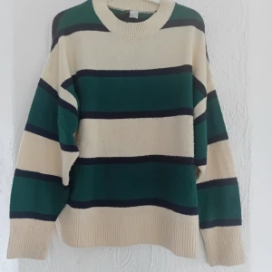 Randig stickad tröja - Säljer en snygg stickad tröja med breda ränder i beige, grön och svart. Tröjan har långa ärmar och ribbade muddar vid ärmslut och nederkant. Perfekt för kyliga dagar!