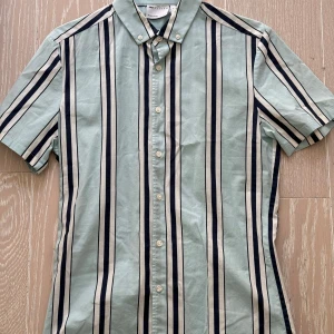 Randig kortärmad skjorta från ASOS DESIGN - Snygg randig skjorta från ASOS DESIGN i ljusgrön och marinblå med korta ärmar. Skjortan har en klassisk krage och knappar framtill. Perfekt för en stilren look.