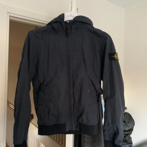 Svart vindjacka från Stone Island - Säljer nu min vindbreaker/Vårjacka från stone Island  då den ej passar längre storleken är 14y men passade mig tills jag blev ungefär 175, jag köpte denna jacka på Nk Stockholm för 2600 och kvitto finns. Den är otroligt stilren och passar till allt, Det är inga defekter på jackan , hör av er vid frågor pris är ej hugget i sten. 