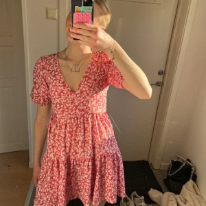 Röd blommig klänning - Charmig röd klänning med blommigt mönster och v-ringning. Den har korta ärmar och en luftig passform som ger en avslappnad känsla. Perfekt för varma dagar. Använd många gånger och köpt för 3 år sedan men är tyvärr lite för kort nu!💓